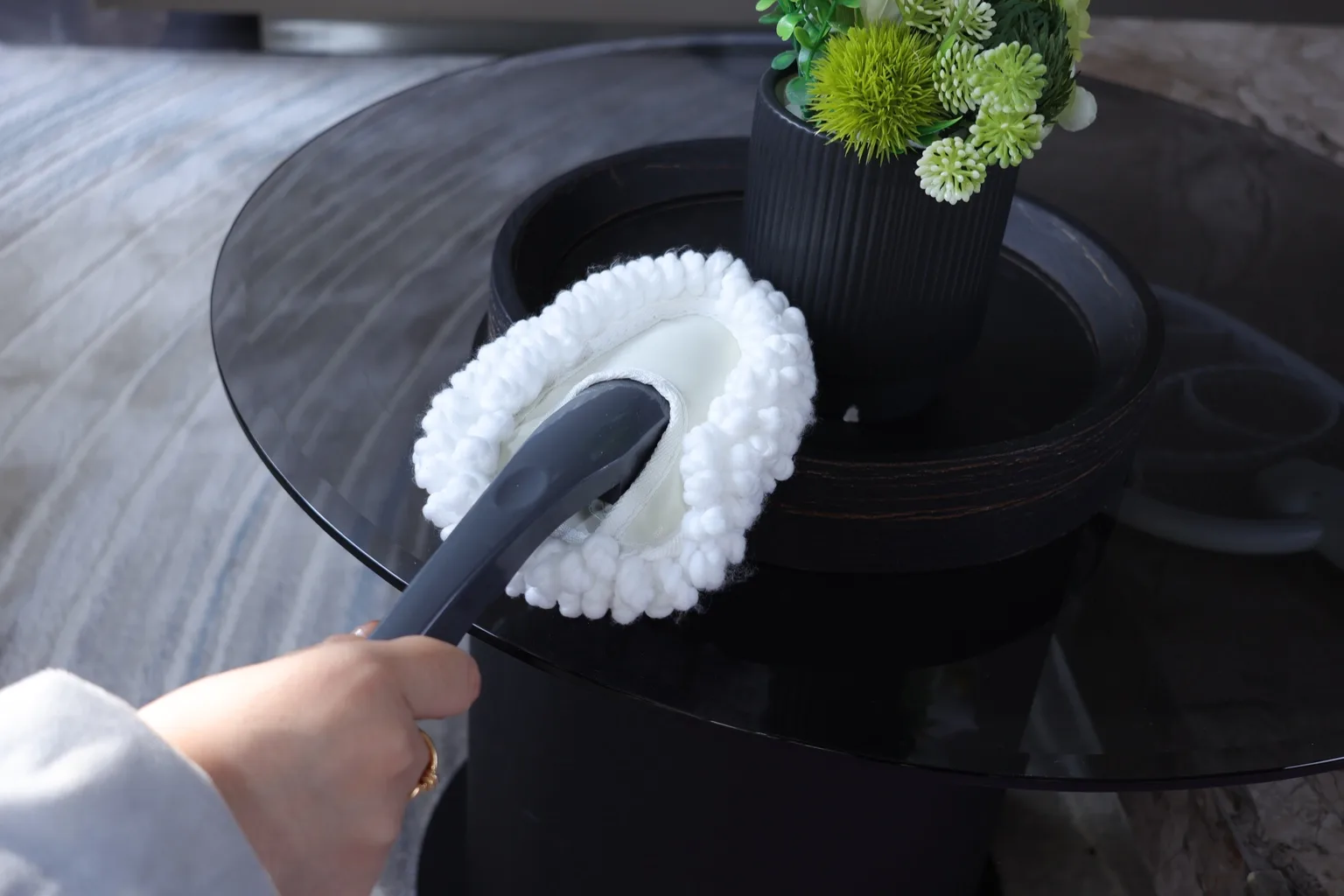 Hand duster cleaning a glass table